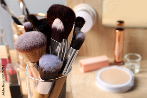 Set of professional brushes and makeup products near mirror on wooden table, closeup. Space for text