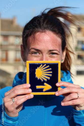 Young beautiful female pilgrim's portrait posing with the typical "Camino de Santiago" blue tile painted with a yellow shell and arrow.