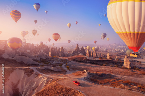 Red car cabriolet in Cappadocia with colorful hot air balloon fly in sky over deep canyons, valleys. Concept banner travel Goreme Turkey