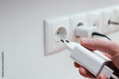 Man hands plugging the charger into an outlet in the wall, close-up. Hand turns on, turns off charger in electrical outlet on wall