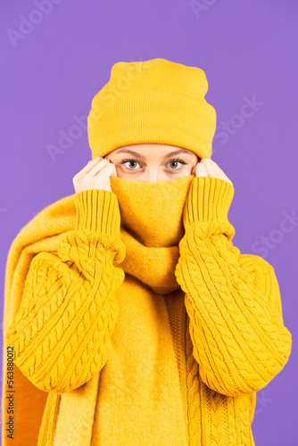 Winter clothing unrecognizable woman covering face with scarf while looking at camera isolated on purple background