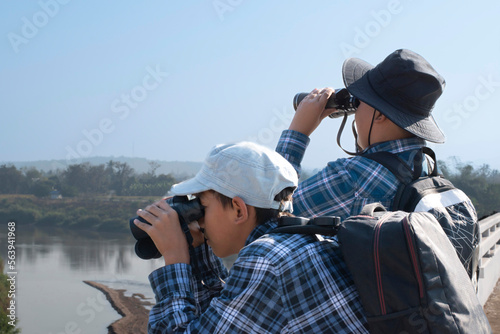 Asian boys are using binoculars to do the birds' watching in tropical forest during summer camp, idea for learning creatures and wildlife animals and insects outside the classroom.