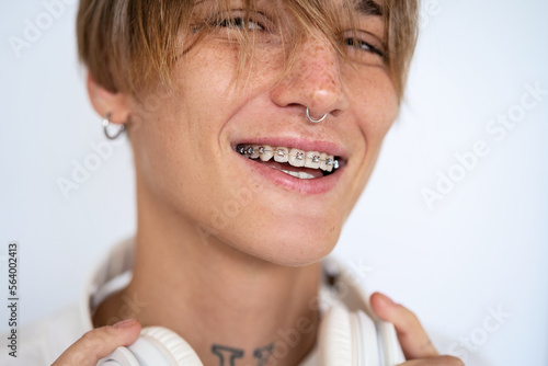 Portrait stylish blonde short haired woman with facial piercing and dental braces looking at camera and smiling against white background.