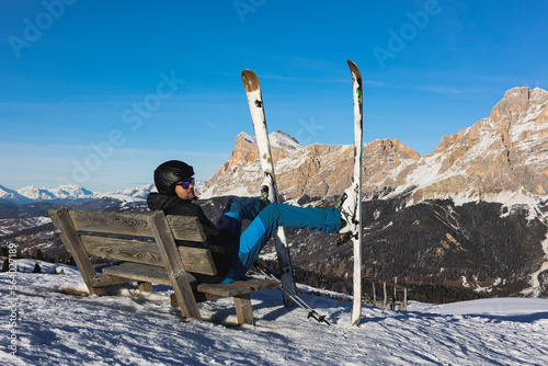 Skier resting on a bench overlooking the Italian Dolomites mountains. Ski, winter sport. Narciarz odpoczywa na ławce i podziwia włoskie góry Dolomity. Narty, sporty zimowe.