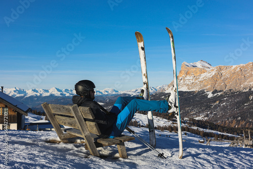 Skier resting on a bench overlooking the Italian Dolomites mountains. Ski, winter sport. Narciarz odpoczywa na ławce i podziwia włoskie góry Dolomity. Narty, sporty zimowe. Pralongia.