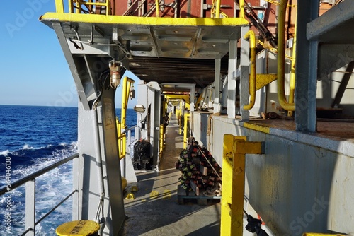 View on main deck and lashing platforms of container vessel painted gray with yellow marking of dangerous obstructions. On deck is secured rope pilot ladder and on the left is calm sea under blue sky.