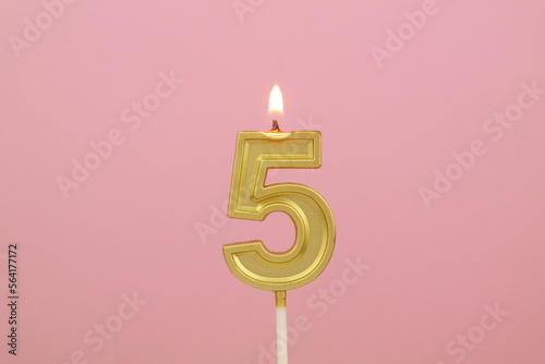Burning gold birthday candle on pink background, number 5