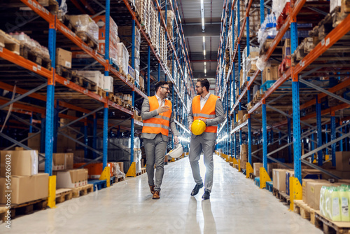 Two associates walks in warehouse full of goods and talks about commodity reserves.