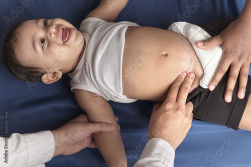 doctor's hands taking femoral pulse on smiling baby