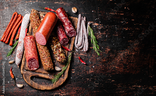 Different types of salami sausage on a cutting board with rosemary. 