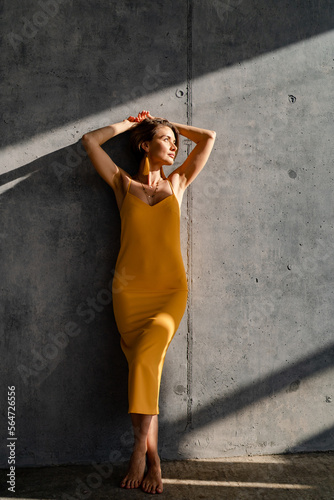 attractive woman in yellow summer dress in interior room concrete wall background