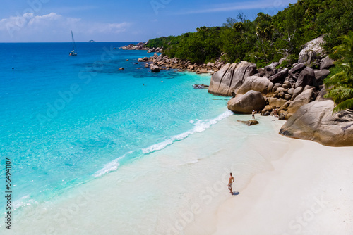 young men on a white beach with turquoise colored ocean, Drone view from above at Anse Lazio beach Praslin Island Seychelles.