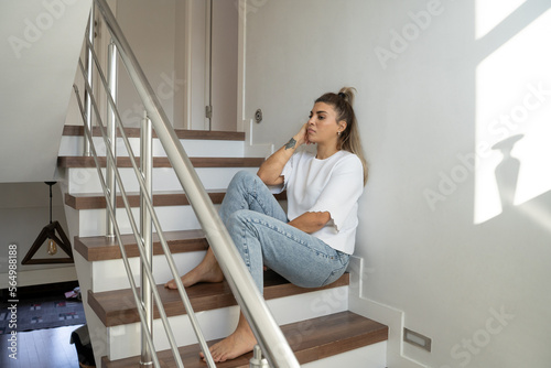 Vertical Portrait Of Brazilian Woman In Depression Sitting On stairs At Home. Concept Of Female Mental Health Women's Issues
