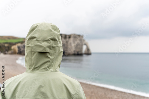 Rückenansicht einer Frau mit Kapuze, die auf Felsen der Normandie blickt 