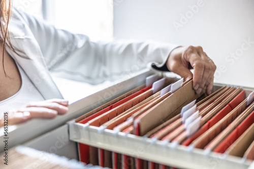 The clerk is leafing through stored folders, looking for a file or document. Concept of data storage, filing cabinet and business administration.