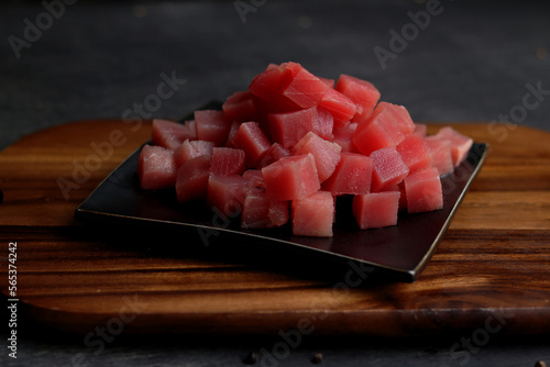Raw tuna cube on black plate.
