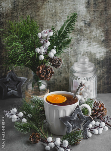 Tea with fruit in a white ceramic cup surrounded by green branches of spruce and pine, berries and fruits. Cozy and stylish winter still life