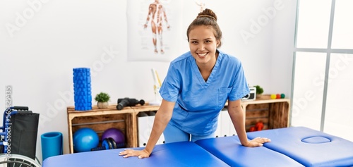 Young beautiful hispanic woman physiotherapist smiling confident standing at rehab clinic