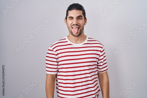 Hispanic man with long hair standing over isolated background sticking tongue out happy with funny expression. emotion concept.
