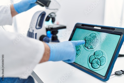 Middle age grey-haired man wearing scientist uniform looking embryology image touchpad at laboratory