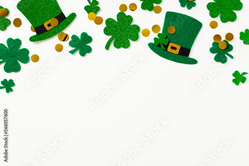 Happy St Patrick's Day flat lay composition. Frame top border made of four leaf clover, gold coins, leprechauns hats on white background.