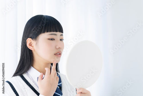 鏡を見て肌荒れを気にする女子学生