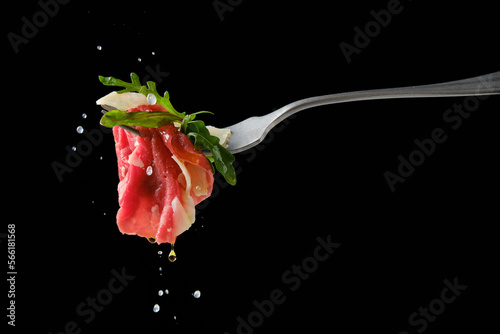 Sprinkling piece of beef carpaccio on fork with lemon juice over black background