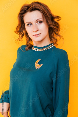 A golden brooch in the form of a month on a green blouse of a brunette girl. Young woman posing on yellow background