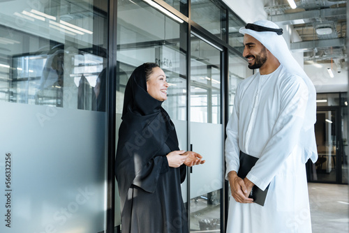 Man and woman with traditional clothes working in a business office of Dubai. Portraits of successful entrepreneurs businessman and businesswoman in formal emirates outfits.