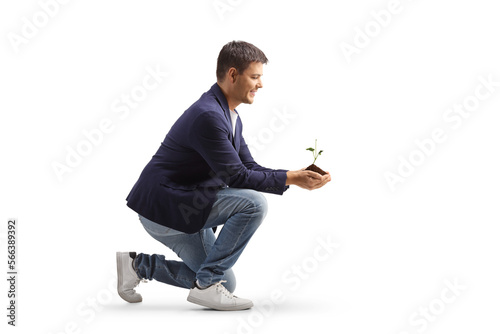 Man kneeling and holding a young plant and earth in his hands