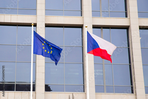 EU flag and Czech Republic flag on flagpole on modern consulate building. Flag of European Union and Czech flag on glass blue facade.