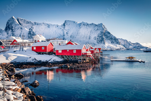 Red wooden houses on the shore of Norwegian sea. Attractive morning scene of popular tourist destination - Lofoten Islands archipelago, Sakrisoy fishing village. Traveling concept background..