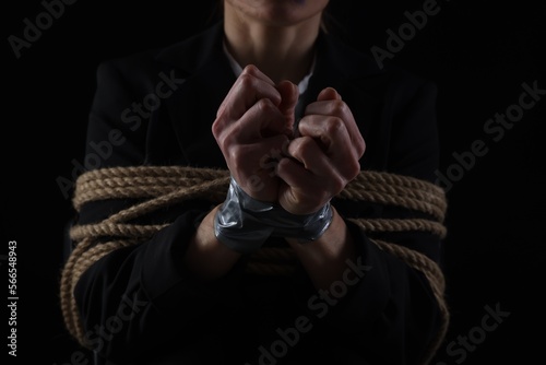 Woman tied up and taken hostage on dark background, closeup