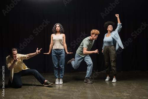 full length of young multiethnic actors rehearsing in different poses on stage of theater.