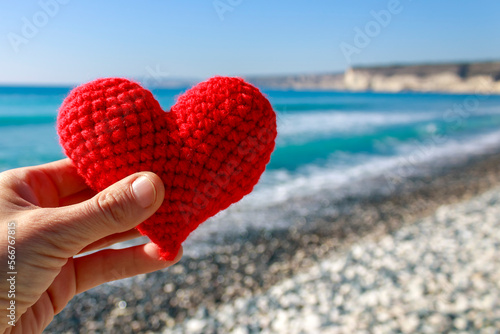 Close-up of red crochet heart in hand on sea beach