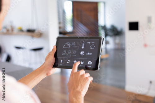 Hands of biracial man at home using tablet with smart home interface on screen