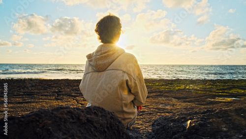 Man on a beach is looking distance during beautiful summer sunset. Human looks to the sun over horizon in the morning while sunrise. Happy person contemplates the beauty of nature. Freedom concept.