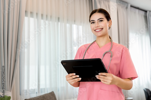 Young processional Caucasian Geriatric doctor in pink scrubs with stethoscope holding digital tablet. Physician in hospital nursing or wellbeing county. Happy caregiver taking care of elderly people.