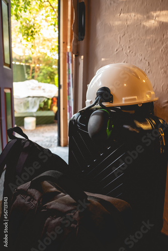 PPE (white safety helmet with attached earmuffs) over a black suitcase and bags at the door in the day