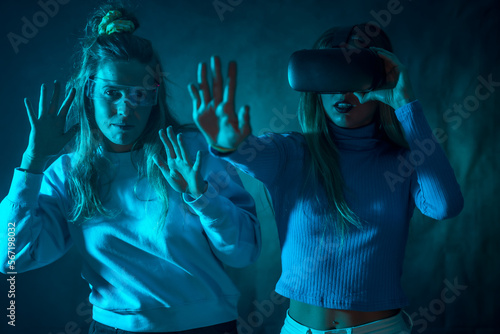 Two futuristic women in vr glasses, playing a game from virtual reality or the metaverse, blue background