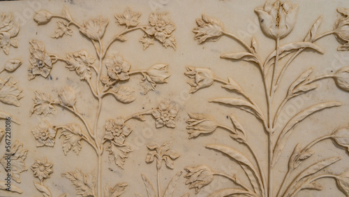 Details of the design of the ancient mausoleum of the Taj Mahal. On the white marble wall there is a relief carving in the form of flowers with elegant stems and buds. India. Agra. Close-up