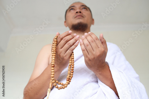 Low angle shot of Asian muslim man wearing white ihram clothes and praying while holding prayer beads