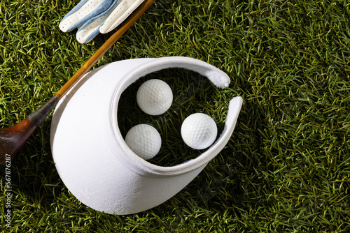 White visor, glove, three golf balls and golf club on grass with copy space
