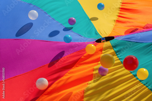 Multicolor-patterned kids play parachute with colorful bouncing balls. Rainbow colors toys for outdoor activities