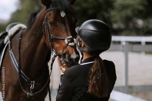 Attractive female equestrian in riding helmet looking at horse in horse club.