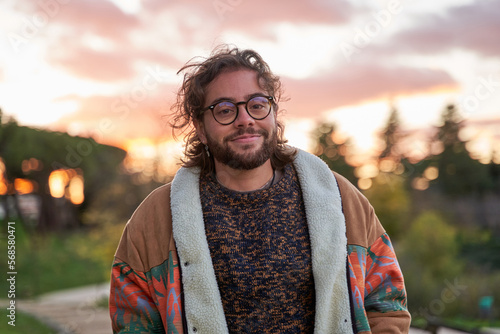 portrait of cheerful trans woman with glasses looking c camera on nature background with a sunset