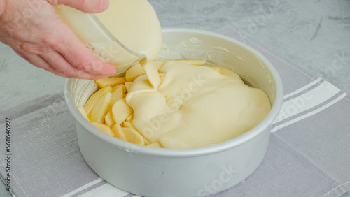 Chef pouring cake batter into a baking pan on the top of apple slices. Apple cake preparation process