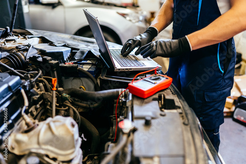 Car mechanic at work. Car an electrician using computer in auto repair shop. Close up.