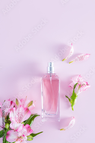 vertical view of the bottle with a spring floral fragrance of women's perfume. delicate pink flowers and buds. lilac background. a copy space.