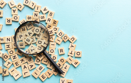 Square letter tiles with magnifying glass against blue background. Search for words and information concept